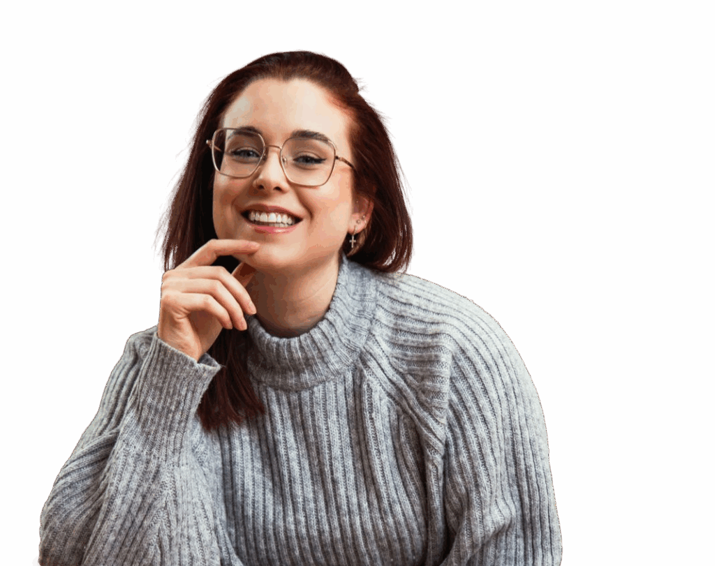 Junge Frau mit Brille und rotem Haar, lächelt und trägt einen grauen, gestrickten Pullover.